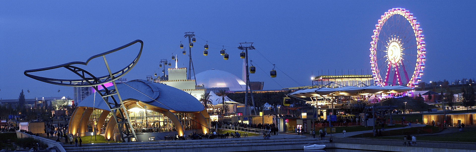 Leuchtende Pavillons, Seilbahn und Riesenrad spiegeln sich am Abend im Wasser der Expo Plaza in Hannover.